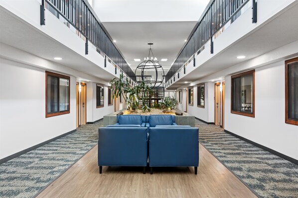A spacious hotel lobby with a central seating area, a staircase, and a large chandelier.