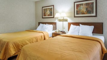 A hotel room with two beds, a nightstand with a lamp, and two framed pictures on the wall.