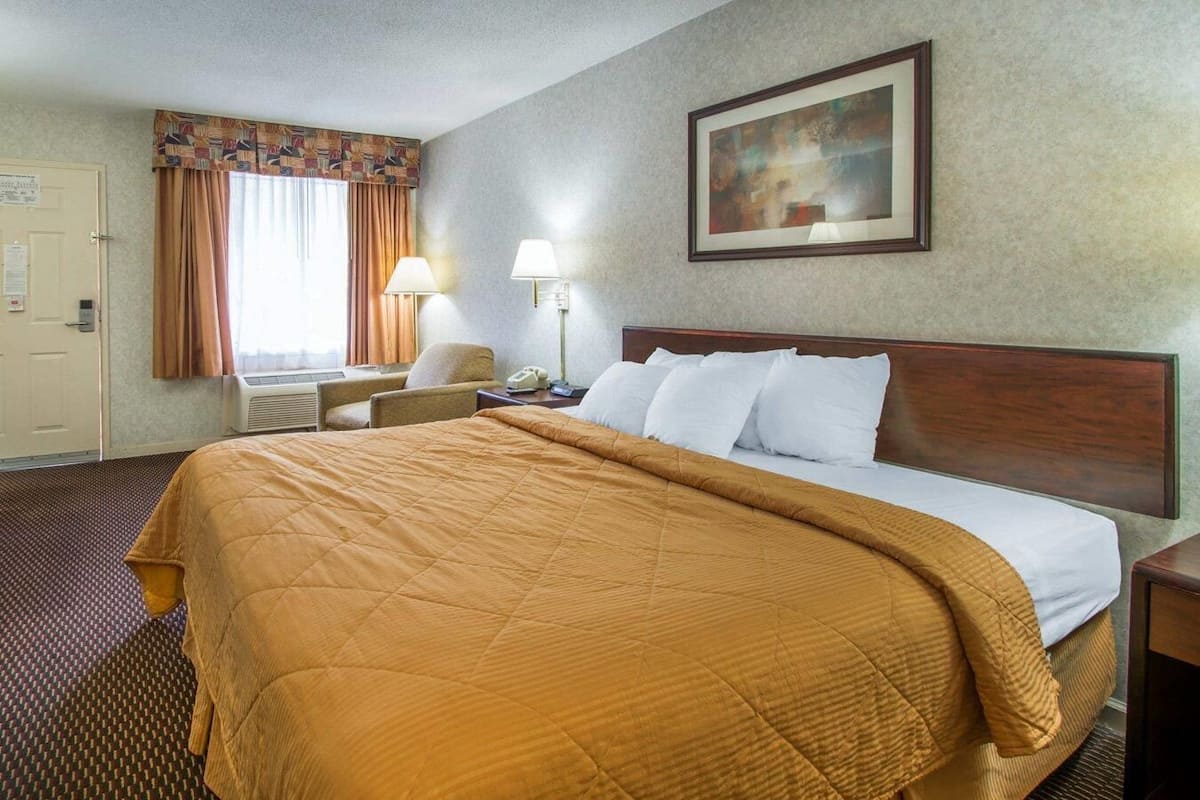 Une chambre d’hôtel avec un grand lit, un bureau, une chaise, une lampe et un tableau au mur.