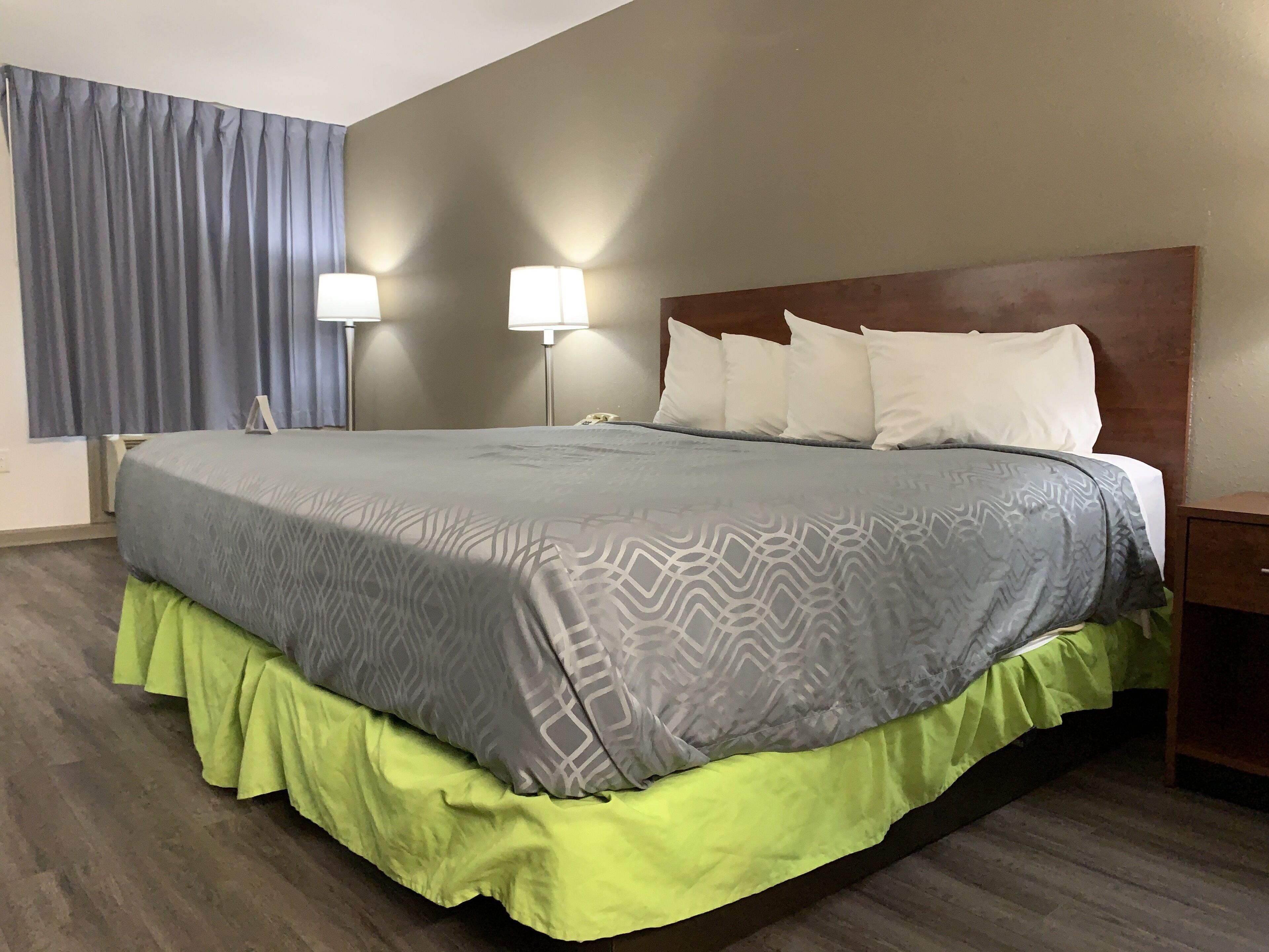 A hotel room with a large bed, two bedside lamps, a wooden headboard, and a telephone on the nightstand.
