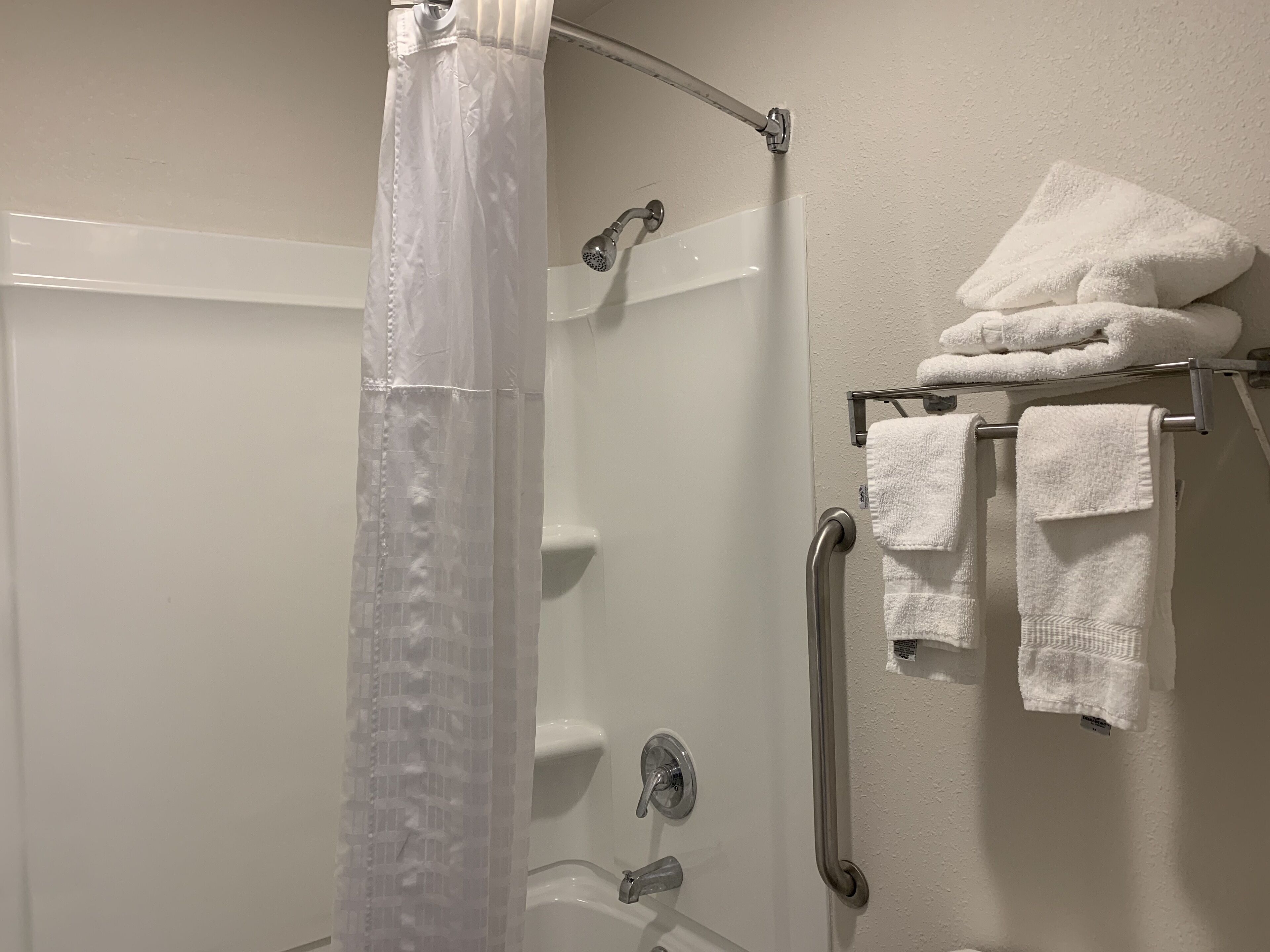 A shower area with a glass door, a handrail, and a towel rack with folded towels.