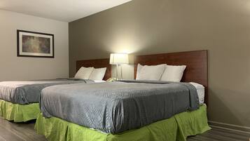 Habitación de hotel con dos camas, cada una con cabecero de madera, ropa de cama estampada en gris y faldas de cama verdes. Se ve una lámpara de noche en una de las camas.