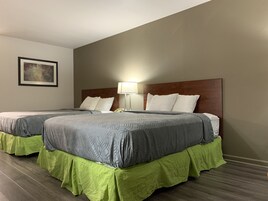 Habitación de hotel con dos camas, cada una con cabecero de madera, ropa de cama estampada en gris y faldas de cama verdes. Se ve una lámpara de noche en una de las camas.