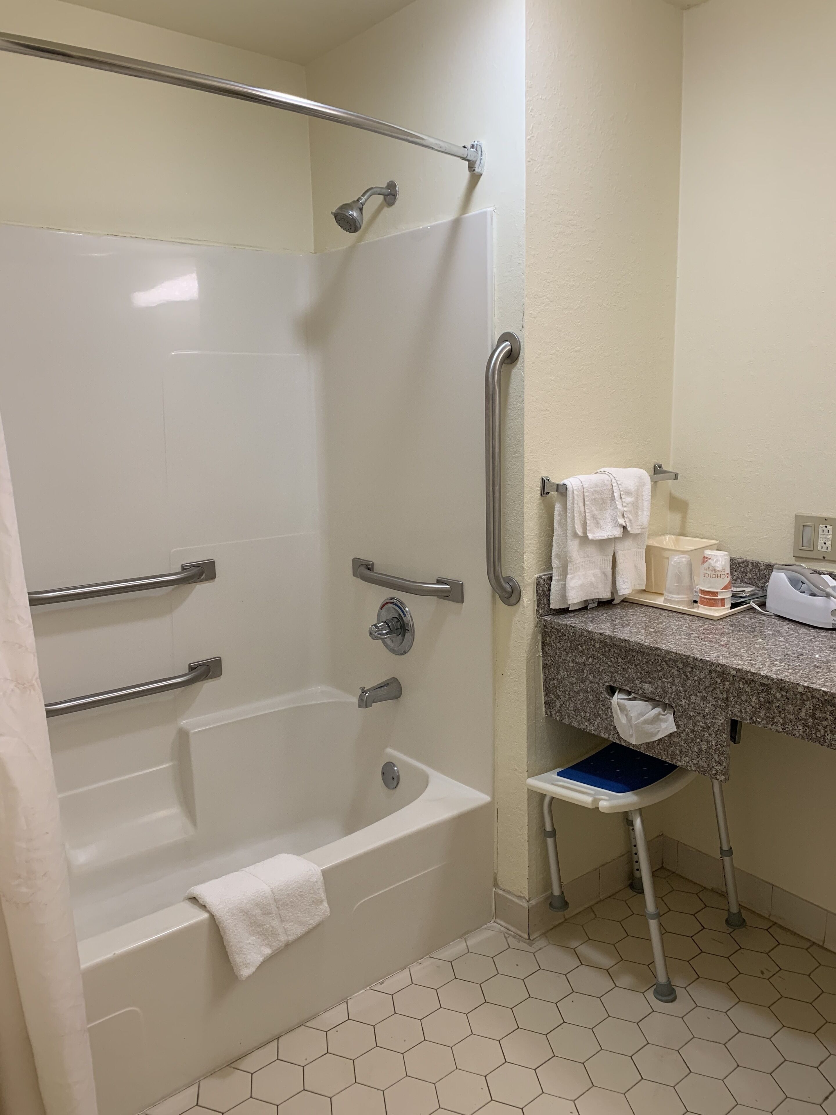 A bathroom with a walk-in shower, grab bars, a bathtub, a sink with a towel rack, and a small step stool.