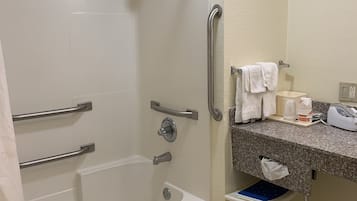 A bathroom with a walk-in shower, grab bars, a bathtub, a sink with a towel rack, and a small step stool.