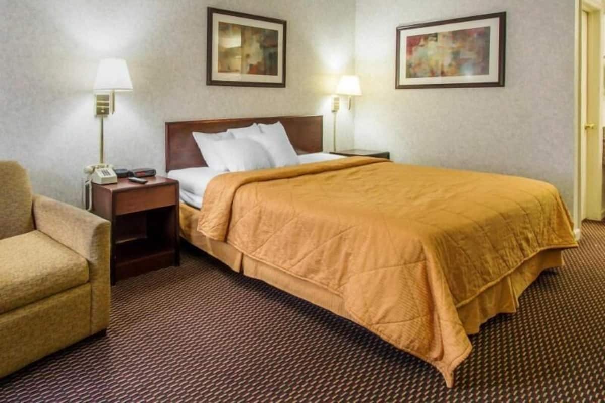 Une chambre d’hôtel comprenant un lit, une table de chevet, une chaise et deux lampes fixées au mur.
