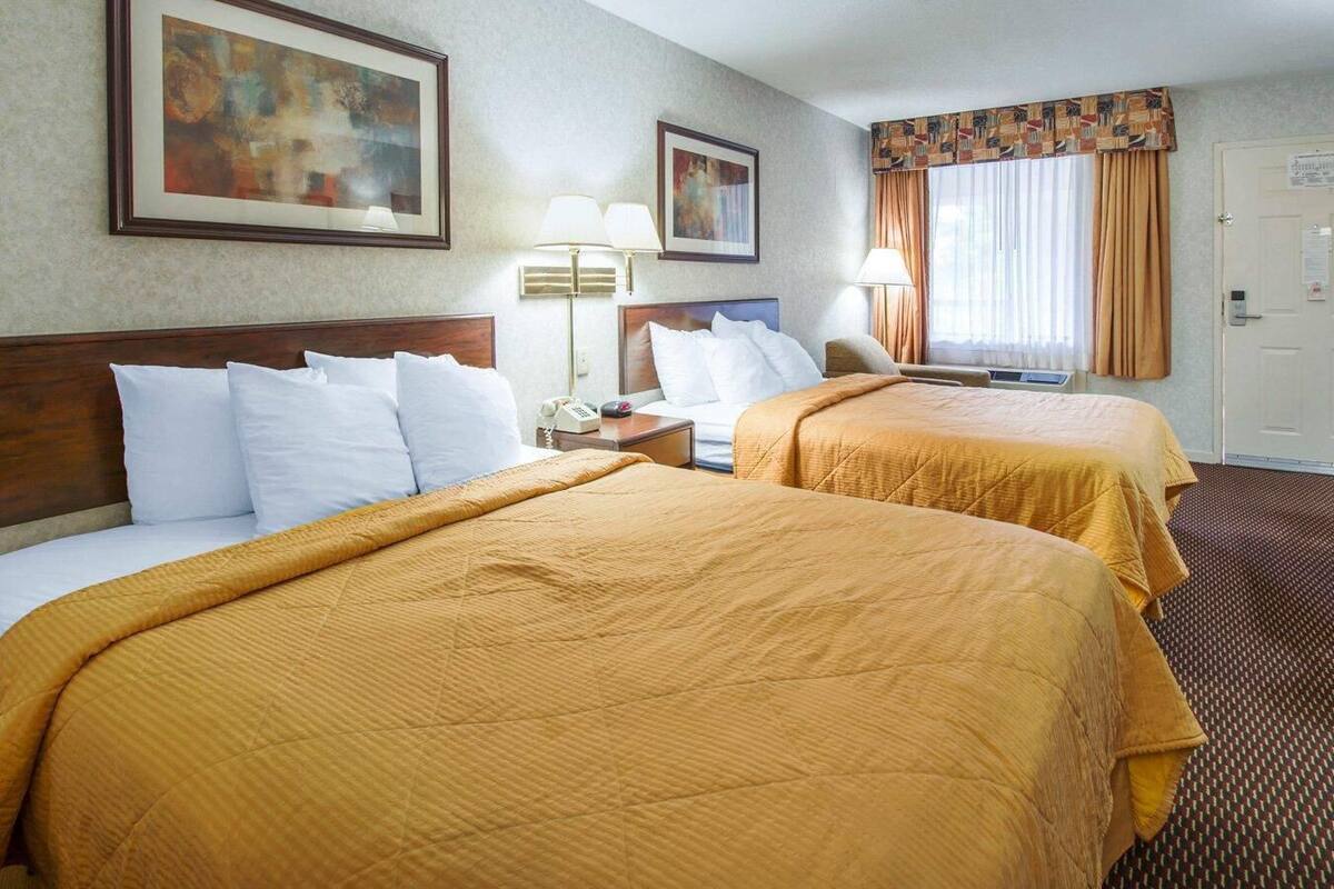 Une chambre d’hôtel avec deux lits, une table de chevet avec une lampe, un tableau au mur et une porte avec une pancarte.