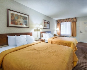 A hotel room with two beds, a nightstand with a lamp, a painting on the wall, and a door with a sign. - Econo Lodge Troy (Troy)