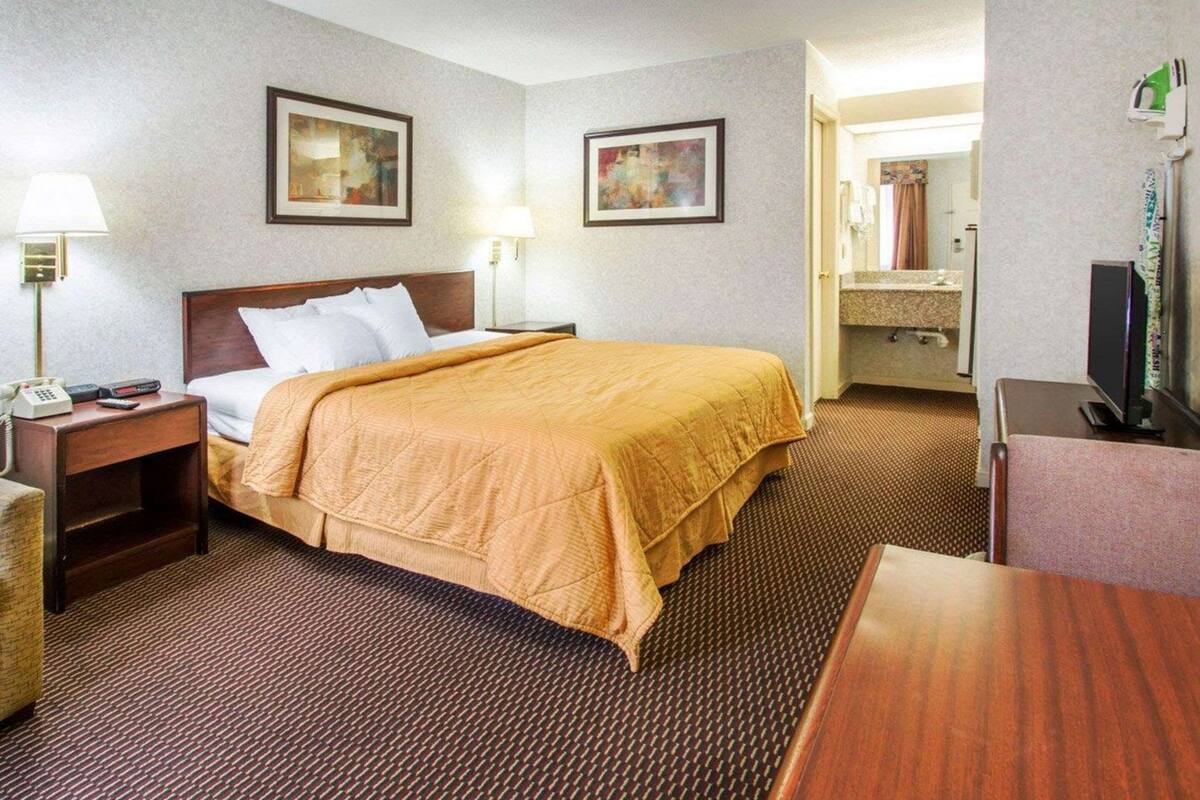 Ein Hotelzimmer mit Bett, Nachttisch, Lampe, gerahmtem Kunstwerk und Fernseher.