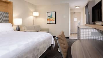 Quarto de hotel com cama, sofá, escrivaninha, cadeira, televisão e um quadro na parede.