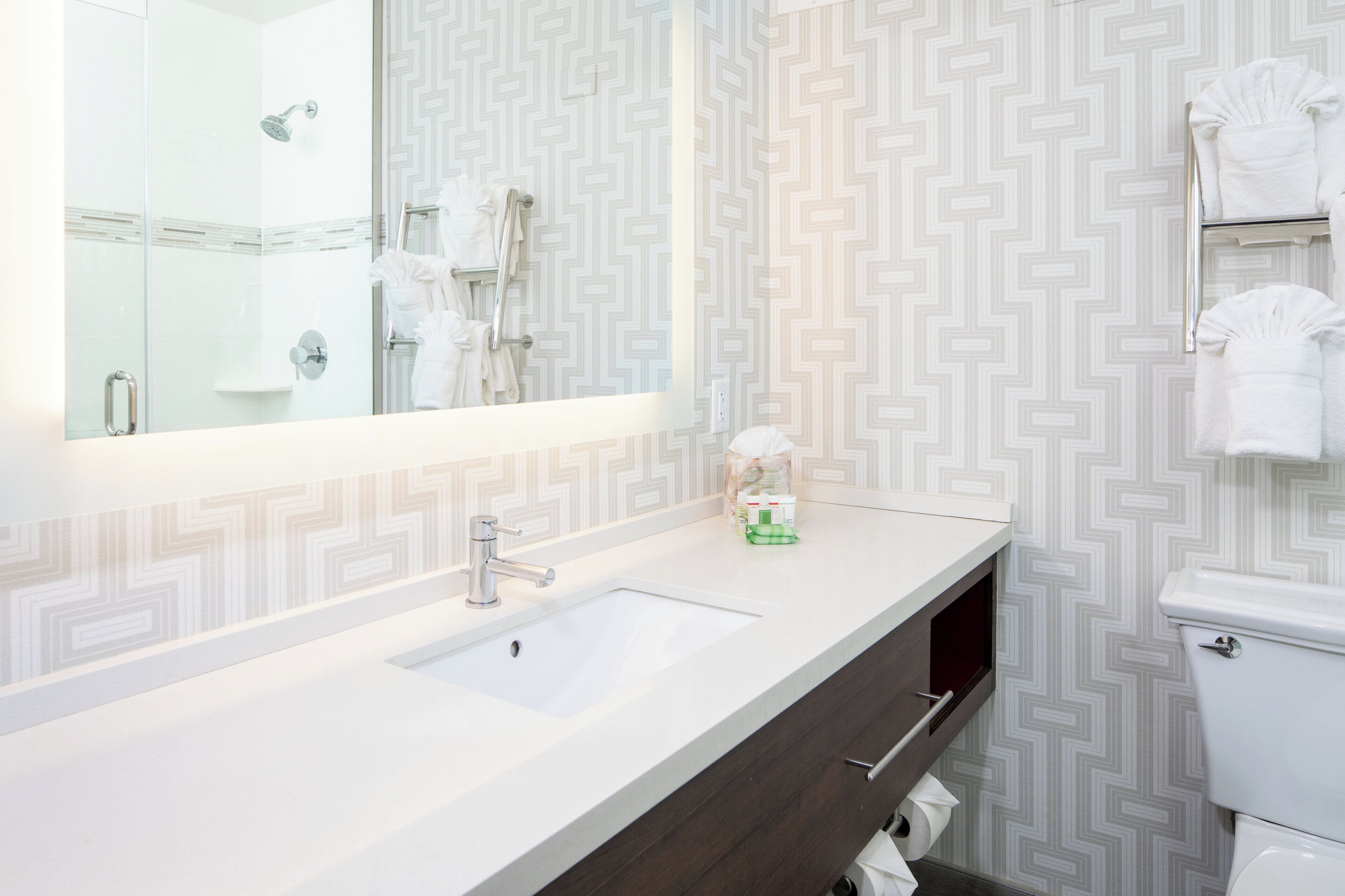 A modern bathroom with a large mirror, a white sink, a dark wooden vanity, and a toilet.