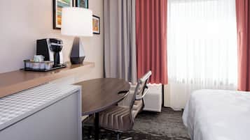 Ein Hotelzimmer mit Bett, Schreibtisch mit Lampe, Stuhl, Kaffeemaschine und Heizkörper.