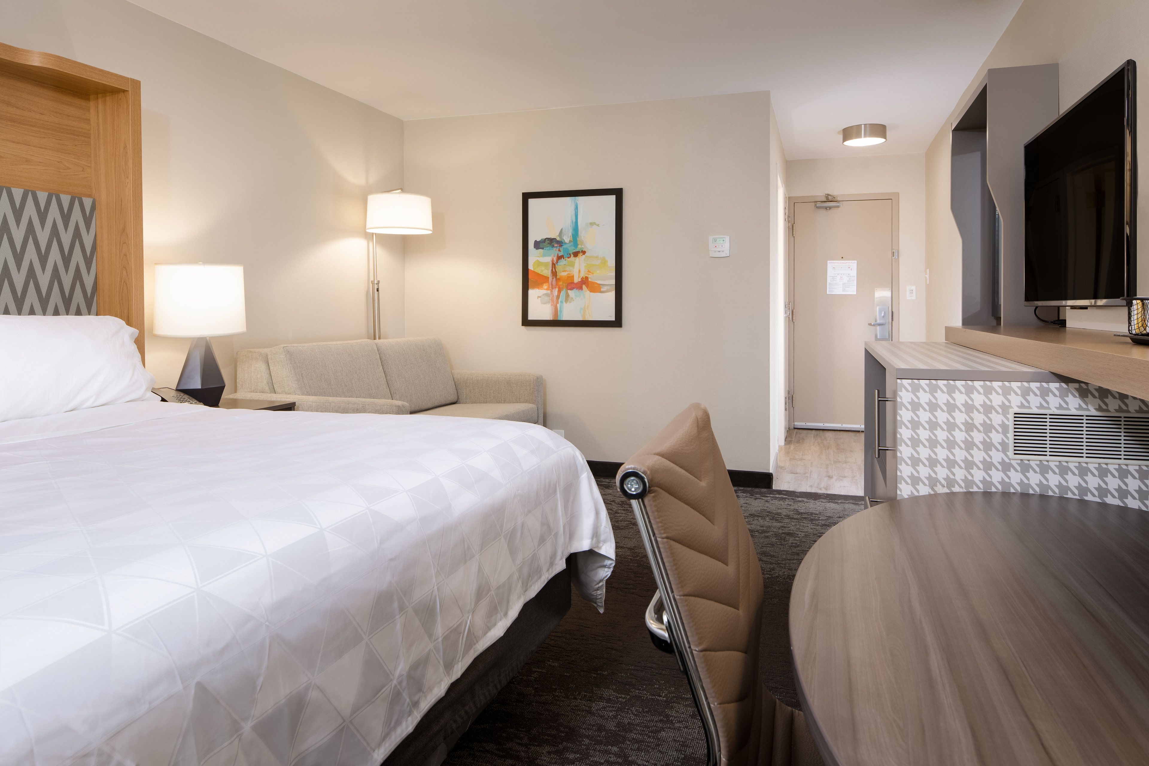 Habitación de hotel con cama, sofá, escritorio, silla, televisor y un cuadro en la pared.