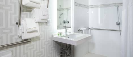 A modern bathroom with a white sink, mirror, and shower. There are multiple white towels on a rack.
