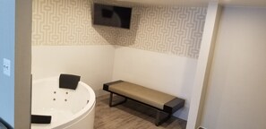 Un baño con bañera, un banco y televisor montado en la pared.