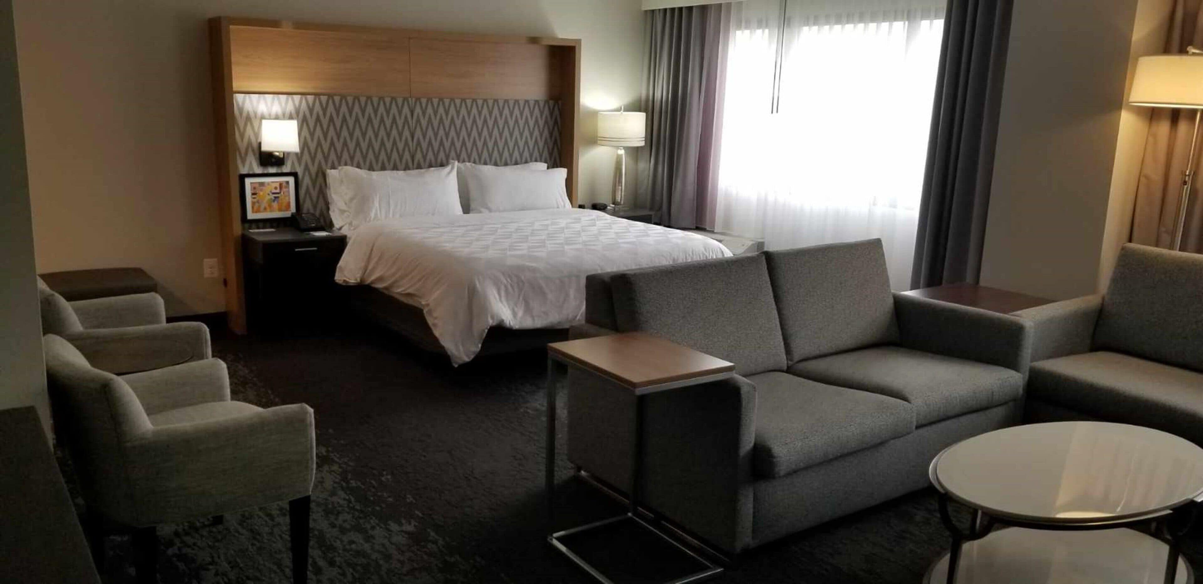 Una habitación de hotel con cama, sofá, mesita, velador y lámpara.