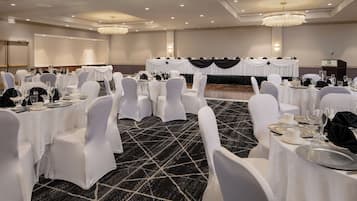 Un salón de banquetes con mesas redondas, sillas blancas y piso alfombrado.