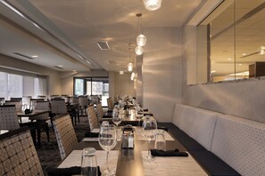 A restaurant with a long dining table, chairs, and hanging pendant lights. - Holiday Inn Washington-College Pk (I-95) by IHG (College Park)