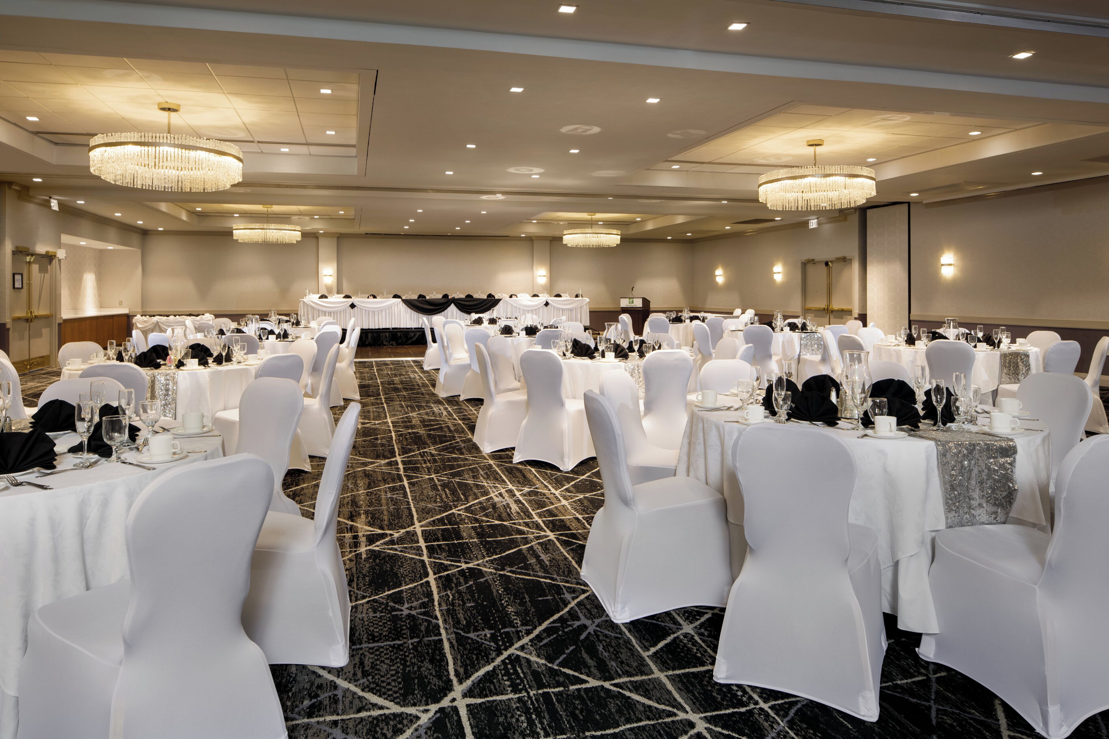 Un gran salón de banquetes con mesas redondas, sillas blancas y candelabros.