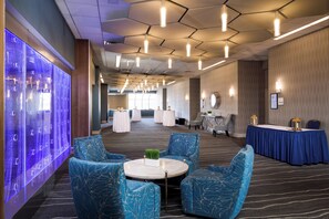 A hotel lobby with round tables, blue patterned chairs, a blue carpet, and a wall with a blue light feature. - Holiday Inn Washington-College Pk (I-95) by IHG (College Park)