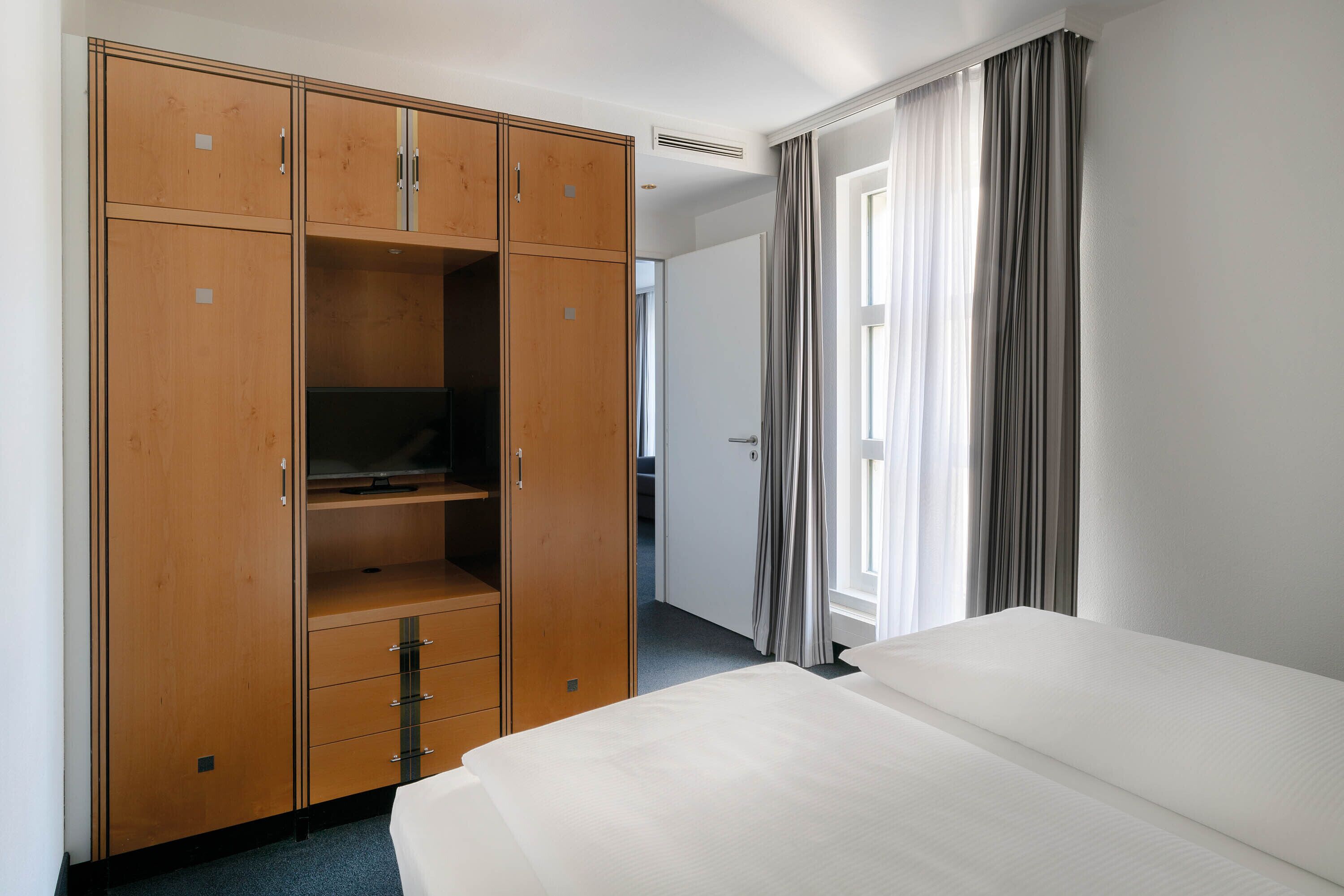Habitación de hotel con un armario amplio, una cama y una ventana con cortinas.