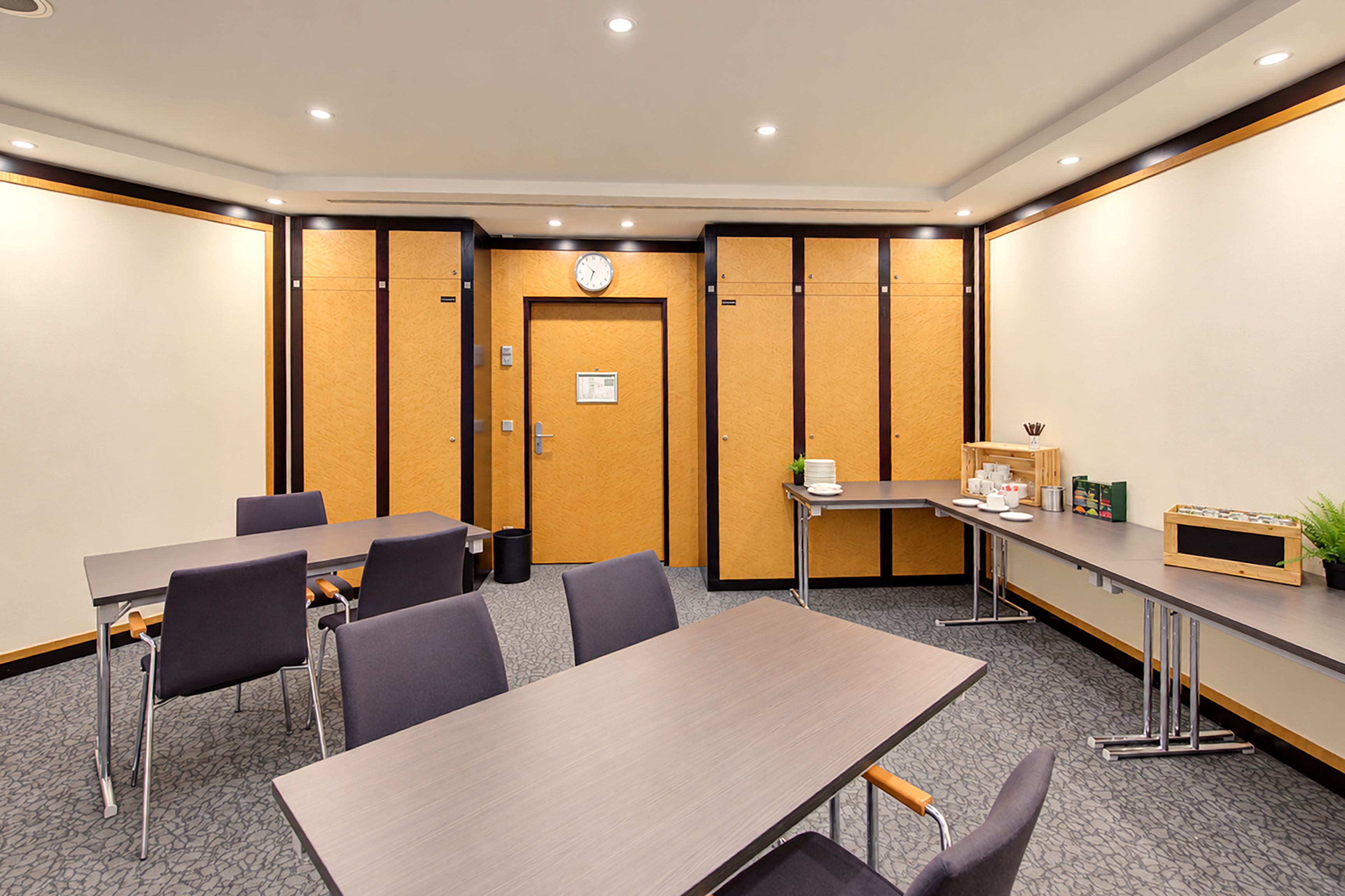 A conference room with a long table, chairs, a clock, and a small kitchenette area.