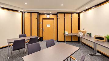 A conference room with a long table, chairs, a clock, and a small kitchenette area.