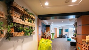 A hallway with wooden planters, a bright yellow bean bag, and a green ottoman. - Seminaris Hotel Leipzig (Leipzig)
