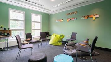 Een kamer met groene wanden, meerdere stoelen, een relaxstoel en een bureau met een computer.