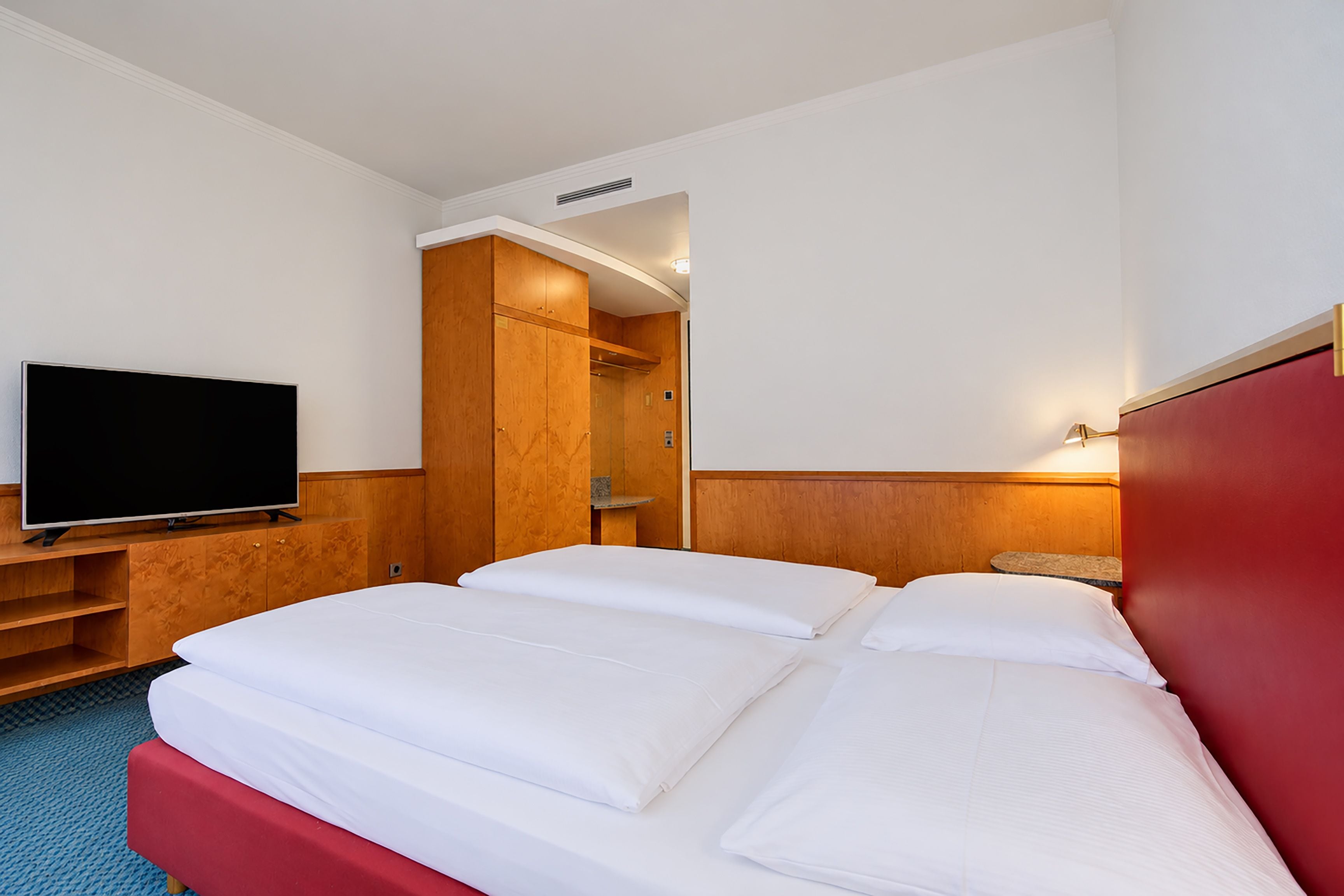 A hotel room with a bed, a television, a wardrobe, and a mirror.