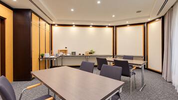 Un salón de conferencias con una larga mesa, sillas, una pizarra y una pequeña planta.