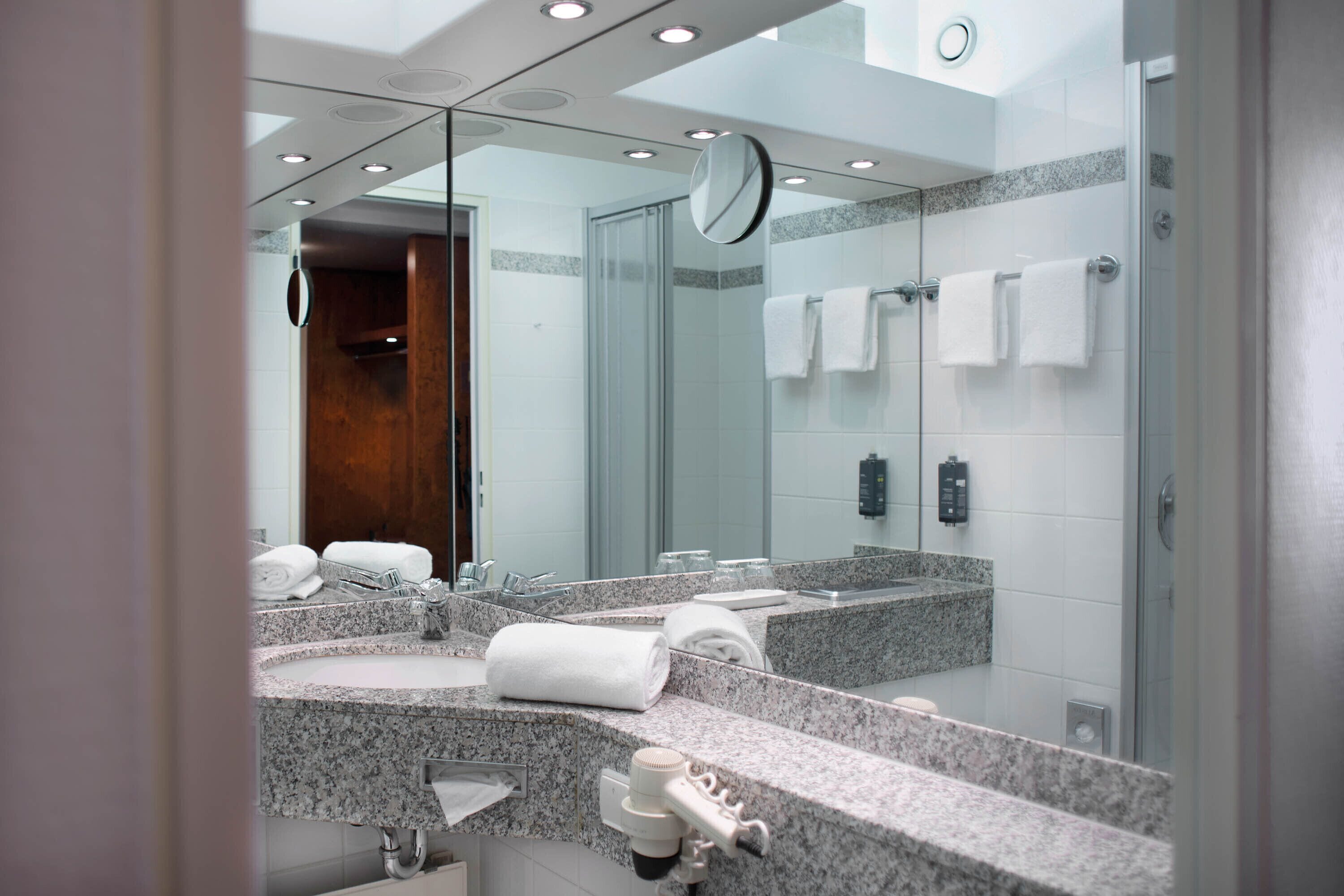 A modern bathroom with a granite countertop, a large mirror, and a glass shower enclosure.
