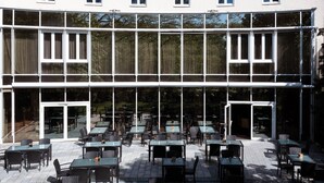 A building with multiple levels, large windows, and outdoor seating areas with tables and chairs. - Seminaris Hotel Leipzig (Leipzig)