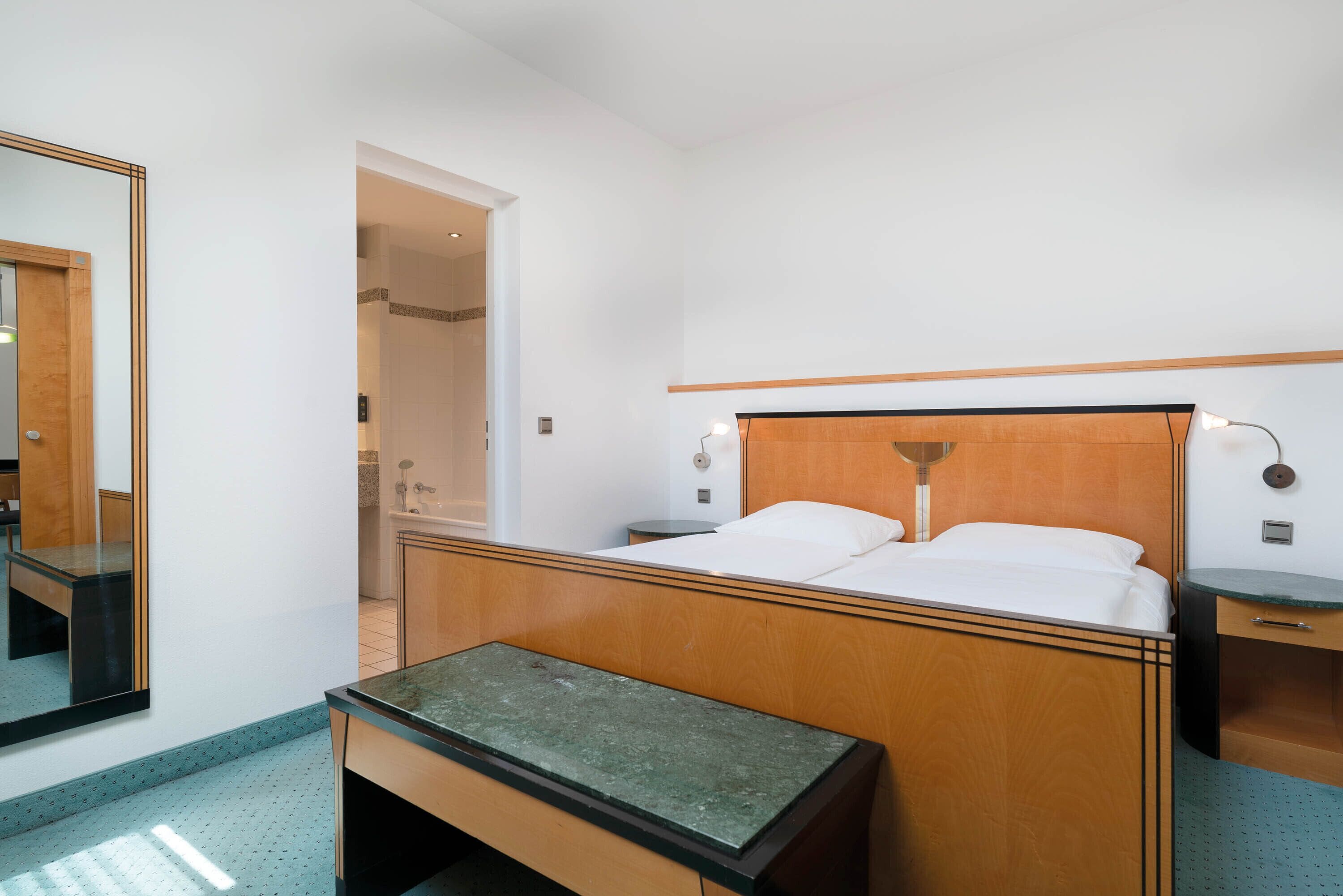 Una habitación de hotel con una cama de madera, una mesita de noche pequeña, un espejo y una mesita auxiliar.