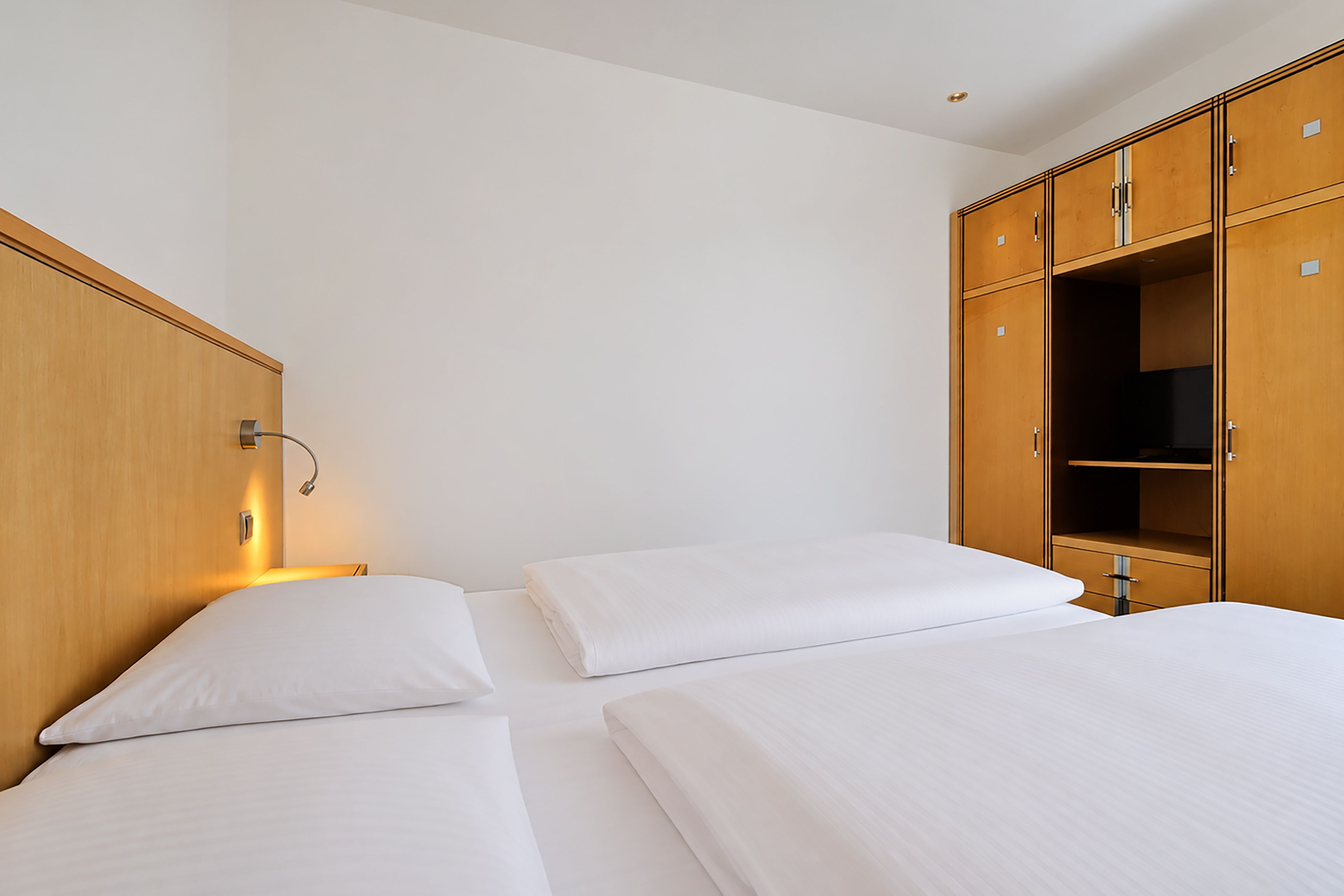 A hotel room with two beds, a wardrobe, and a wall-mounted light.