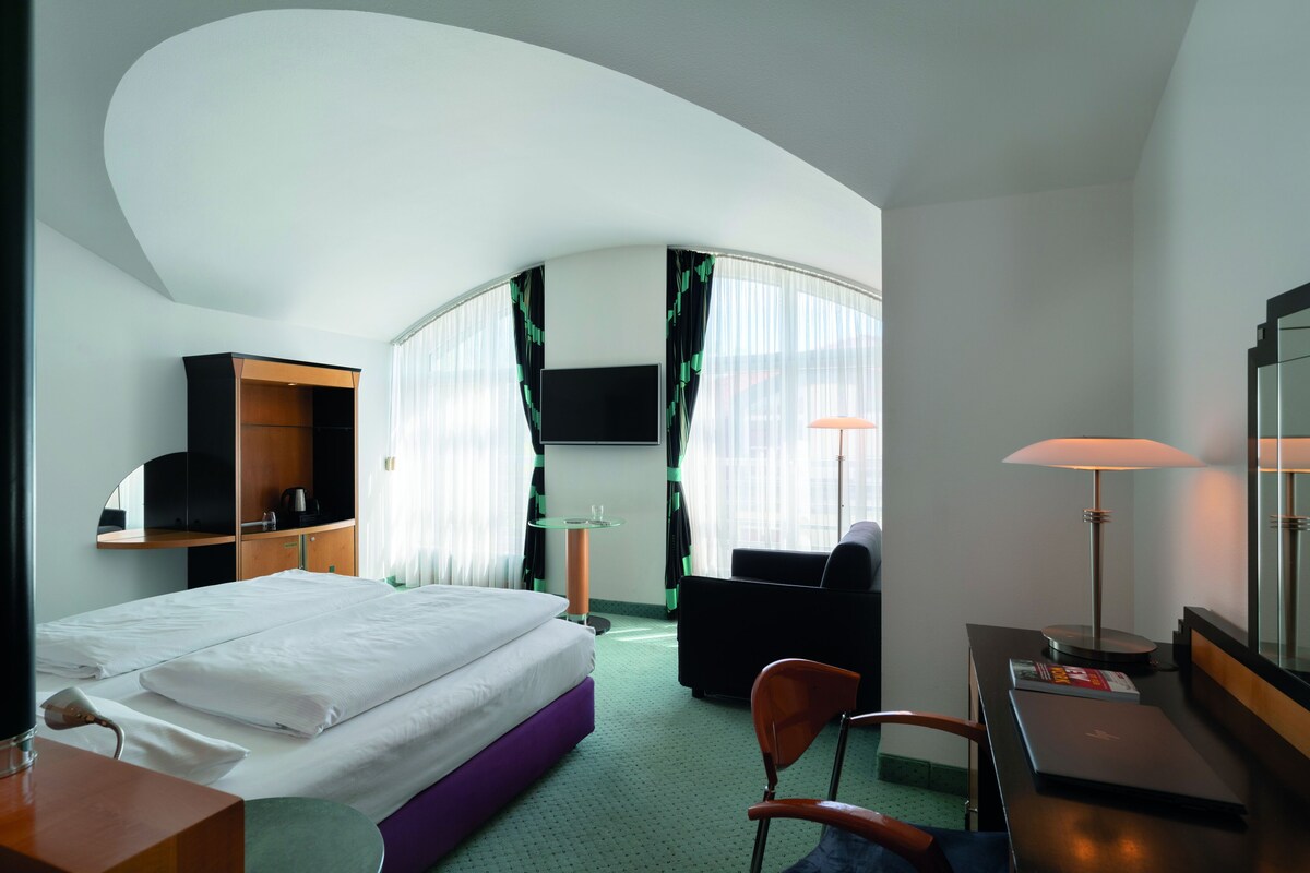 Une chambre d’hôtel avec un lit, un bureau, une chaise, une télévision et une lampe.