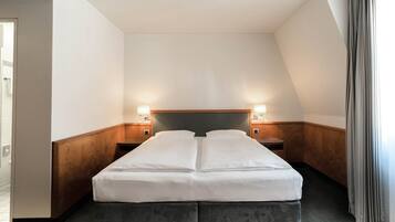 A hotel room with a double bed, two bedside tables with lamps, wooden paneling on the walls, and a view of the outside through a window with curtains.