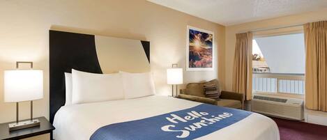 A hotel room with a large bed, a nightstand, a chair, a window with curtains, and a picture on the wall.