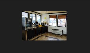 A kitchen with a built-in microwave, a coffee machine, and a small refrigerator. There are large windows providing natural light and a view of the outside.