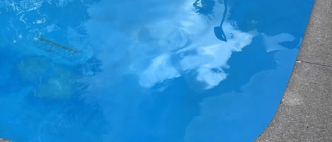 A swimming pool with clear blue water, a tiled deck, and a pool ladder.