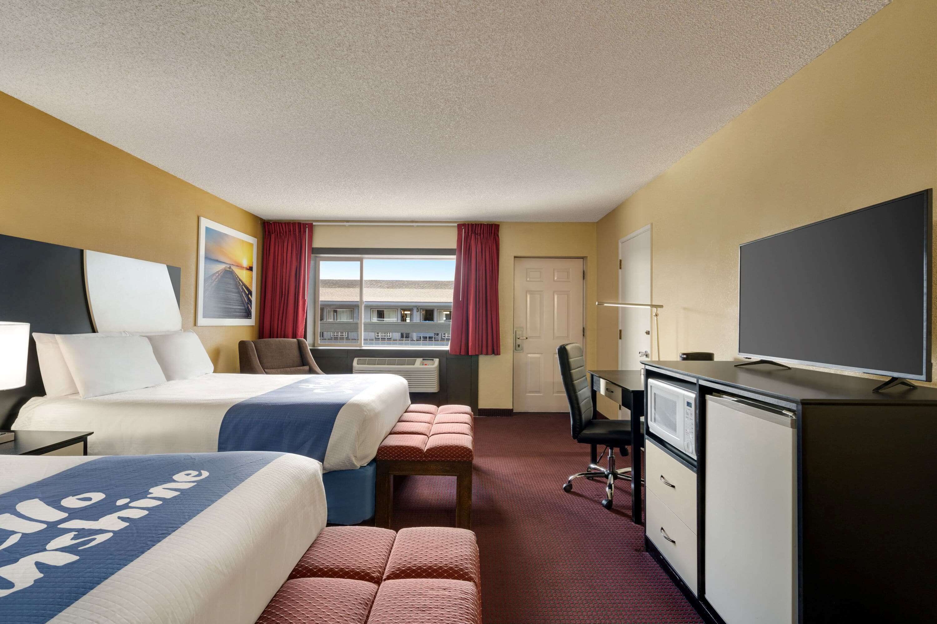 A hotel room with two beds, a desk, a television, and a window with curtains.
