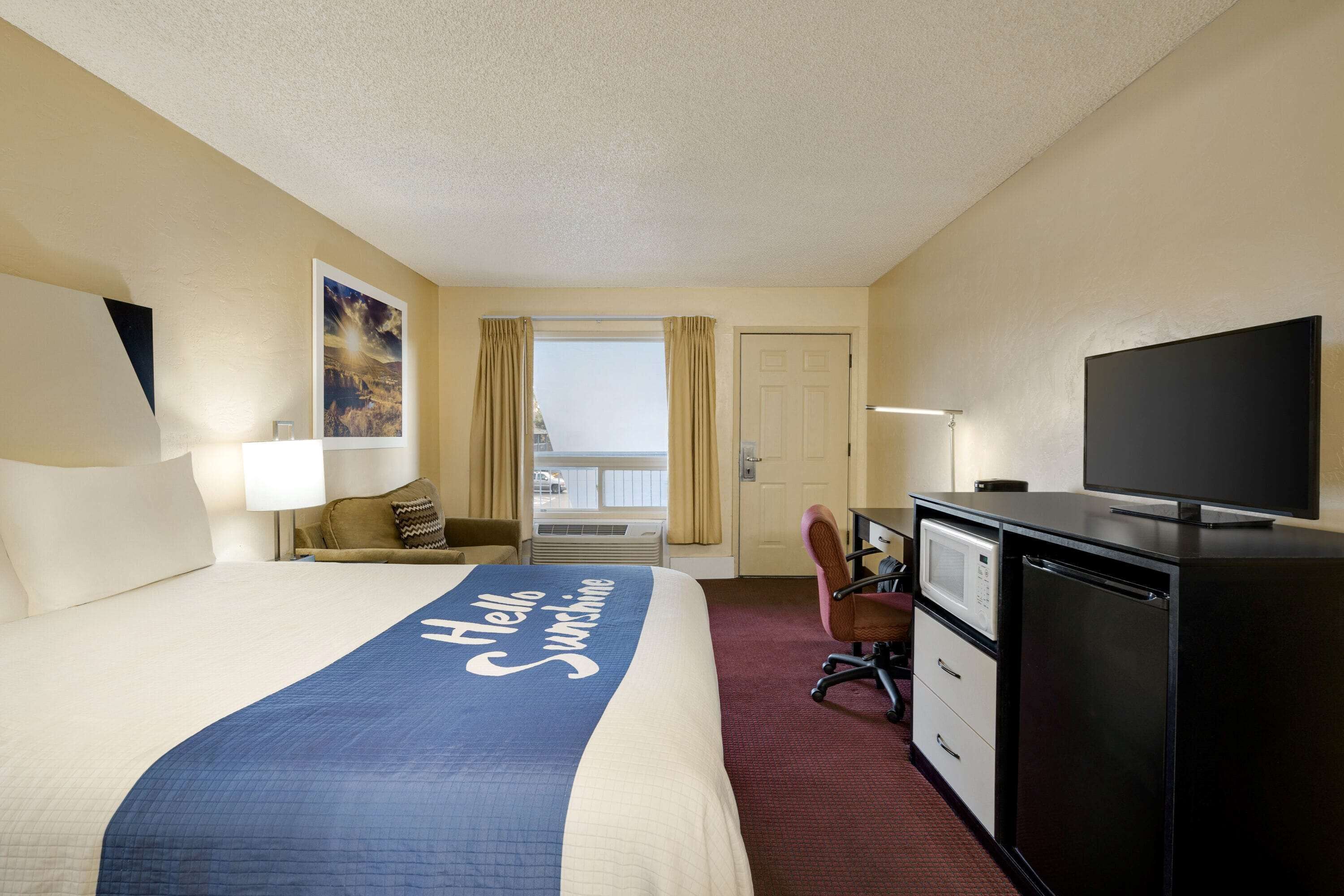 Habitación de hotel con cama, escritorio, televisión y vistas al exterior.