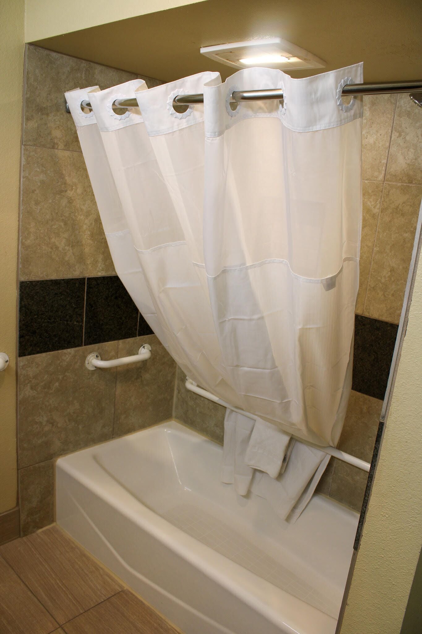 A bathroom with a bathtub, a shower curtain, and a handrail.