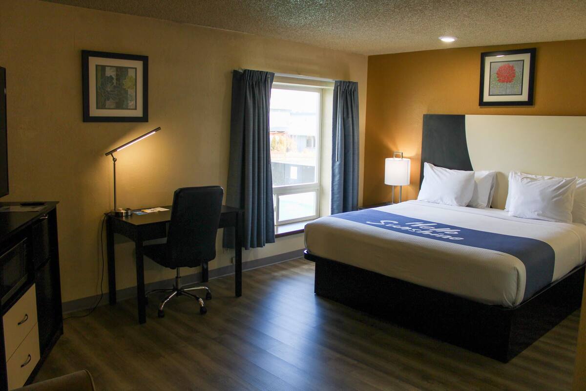 A hotel room with a bed, desk, chair, and two lamps.