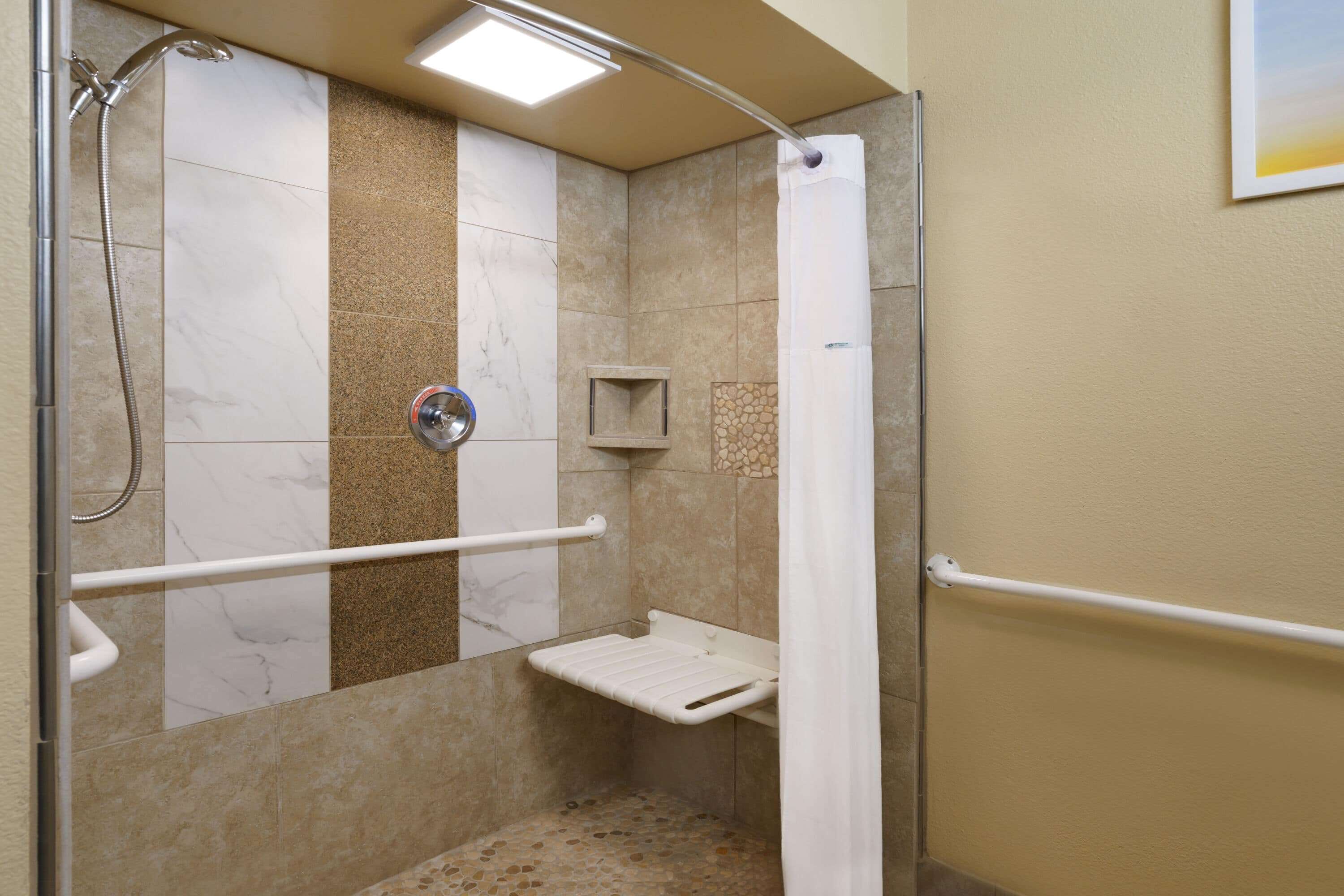 A shower area with a grab bar, a small shelf, and a showerhead.