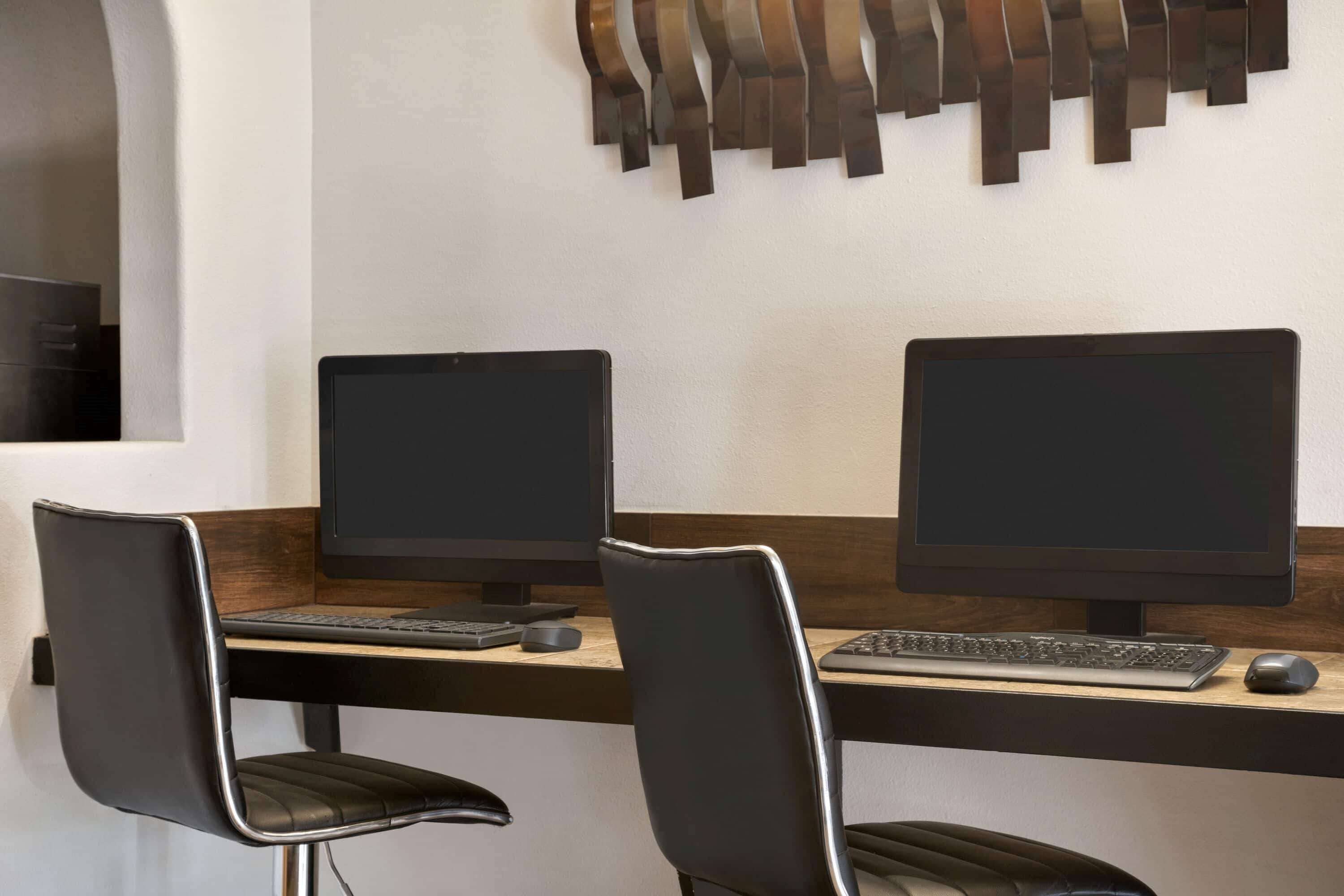 A modern office space with two desks, each with a computer monitor, keyboard, and mouse.