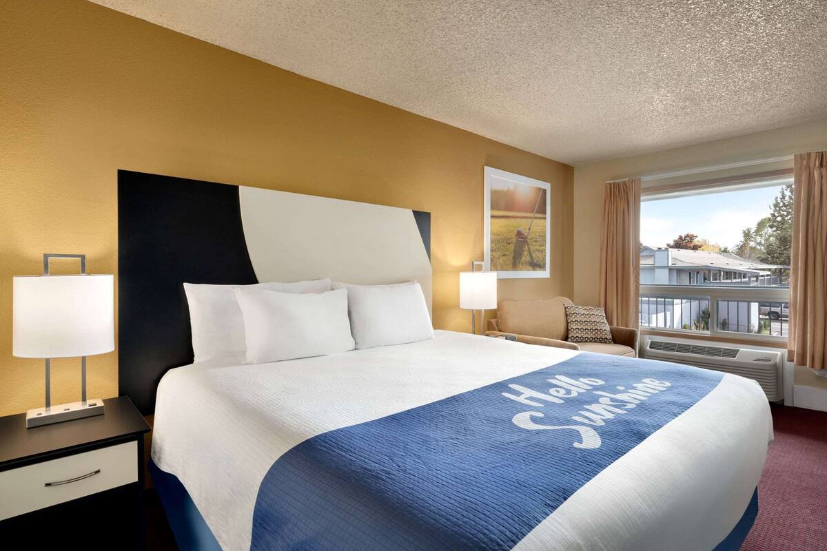 A hotel room with a large bed, two bedside tables, a window with curtains, and a view of the outside.