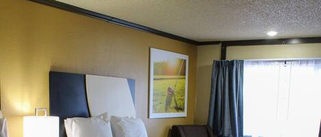 A hotel room with two beds, a desk, a chair, a lamp, and a window with curtains.