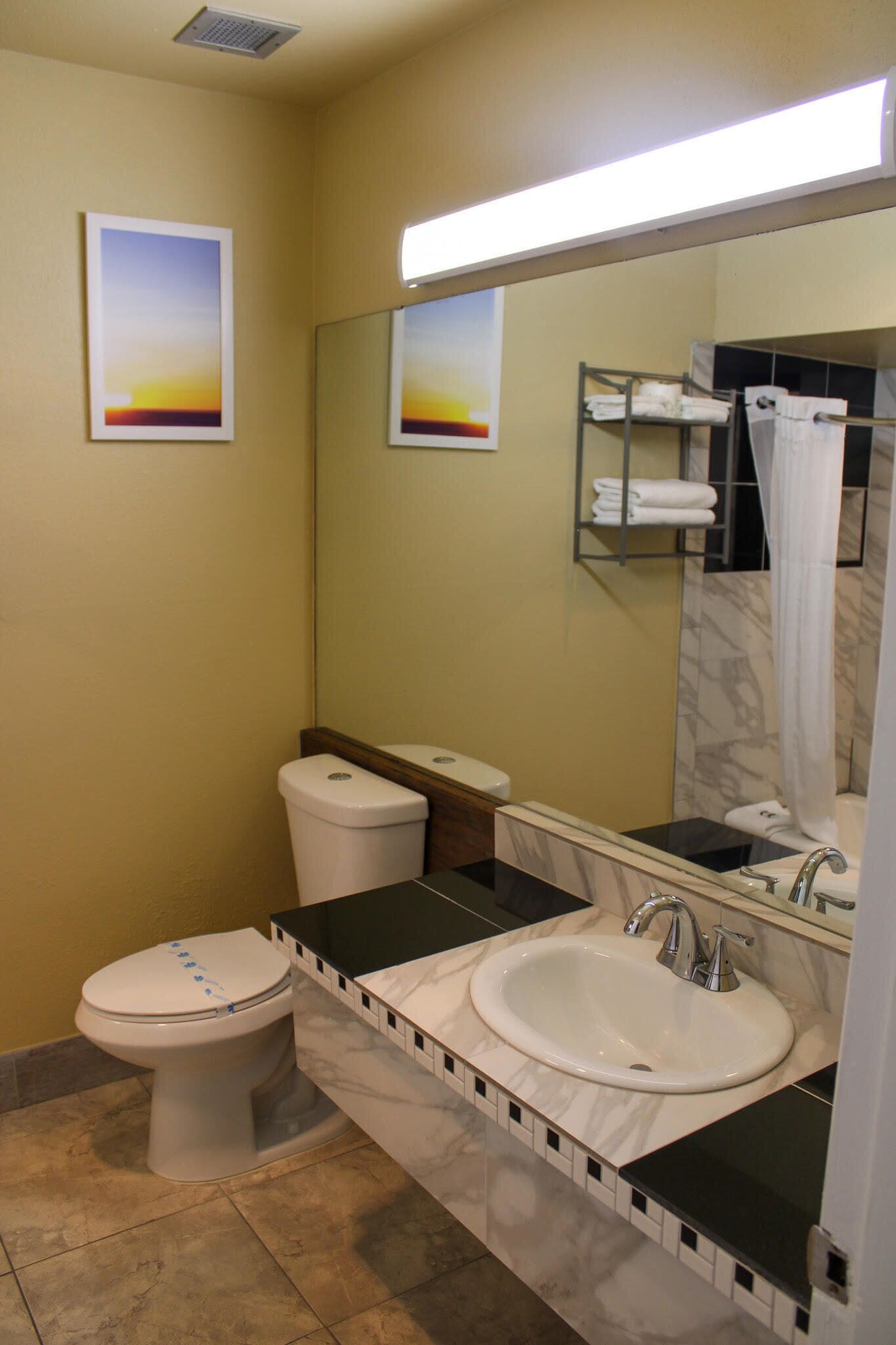 A bathroom with a toilet, sink, and mirror. There are towels on a rack and a shower curtain.