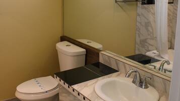 A bathroom with a toilet, sink, and mirror. There are towels on a rack and a shower curtain.